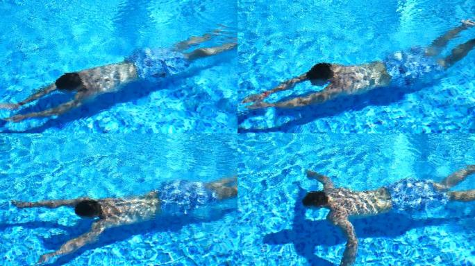 穿着短裤的面目全非的男人在酒店游泳池的水下游泳。暑假期间放松的家伙在酒店的盆地游泳。阳光明媚的时候，