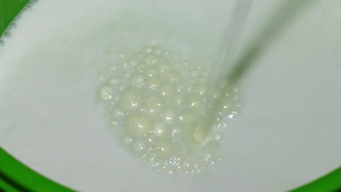 牛奶正在倒入绿色桶中。牛奶从黄色的管子中流成细流。自制黄油的生产。