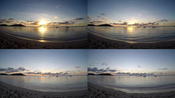 南太平洋热带岛屿上的日落。斐济群岛亚萨瓦群岛纳库拉岛蓝色泻湖海滩上日落光的时间流逝，背景是一些船只