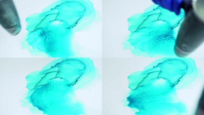 由绿松石丙烯酸漆和水制成的流体抽象画的俯视图特写。吹风机用于在画布上传播颜色