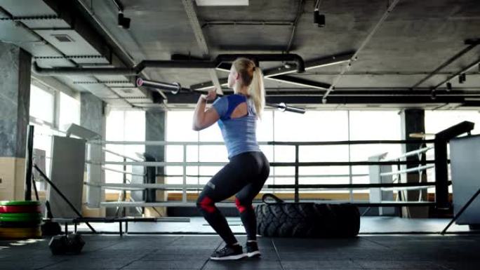 金发女运动员在健身房锻炼时举起杠铃做挺举运动的四分之三后视图