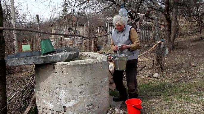 一个荒芜的村庄里的老妇人正在从水桶里的井里取水，独自生活。