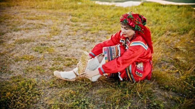 一个穿着俄罗斯民间服装的女人穿着韧皮鞋 -- 坐在球场上。