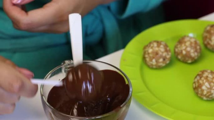 一个女人在融化的巧克力中蘸一个爆米花方坯，然后摇晃。盘子上的下一个是现成的空白。