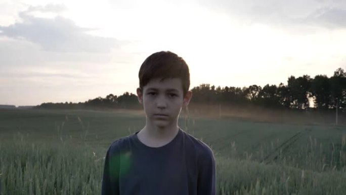 悲伤的男孩抬起眼睛，在日落时看着相机，在户外冒犯了男孩