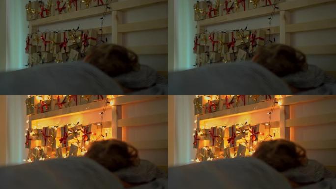 一个小男孩睡在床上，他的床背上闪耀着圣诞彩灯的降临日历。为圣诞节和新年概念做准备。降临日历概念