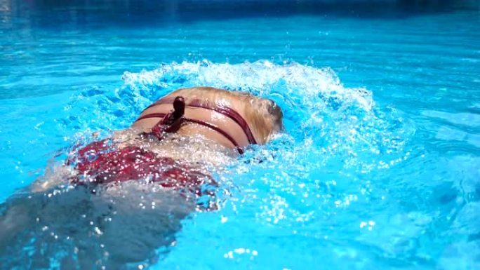 无法辨认的女人在透明清水的水池中潜水。暑假放松的年轻女孩在盆地提神。暑假的概念。慢动作后视图