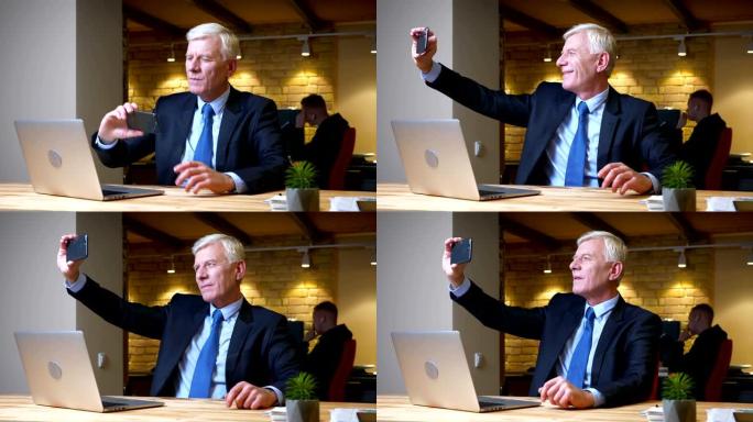 白人老商人在办公室的笔记本电脑前坐在手机上自拍的特写镜头