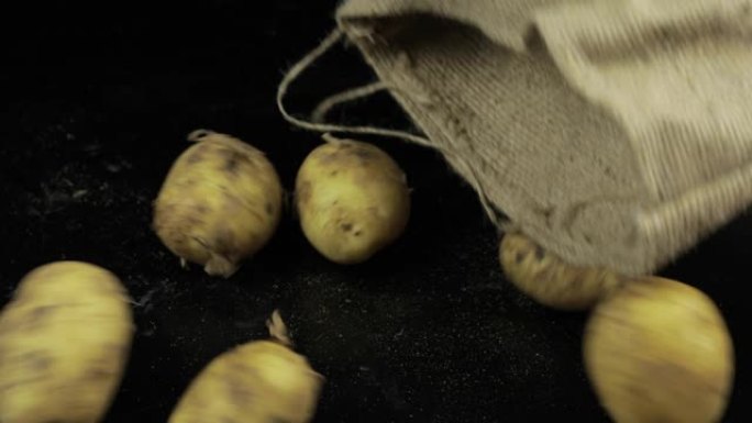 从帆布袋掉在黑色表面上的土豆。一堆新鲜的生土豆