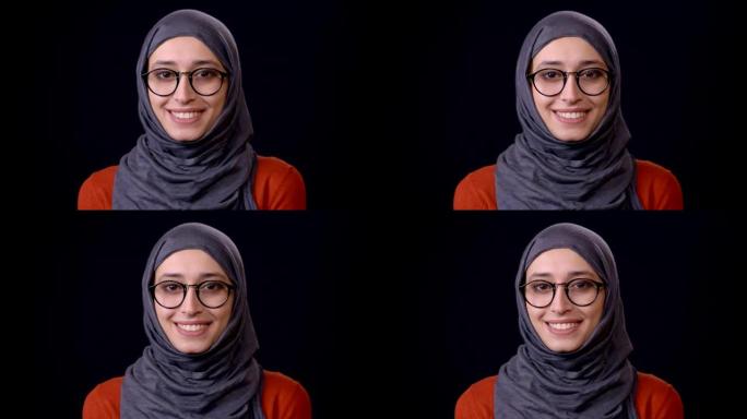 戴着头巾的年轻迷人阿拉伯女性的特写镜头看着相机，快乐地微笑着，背景被孤立在黑色上