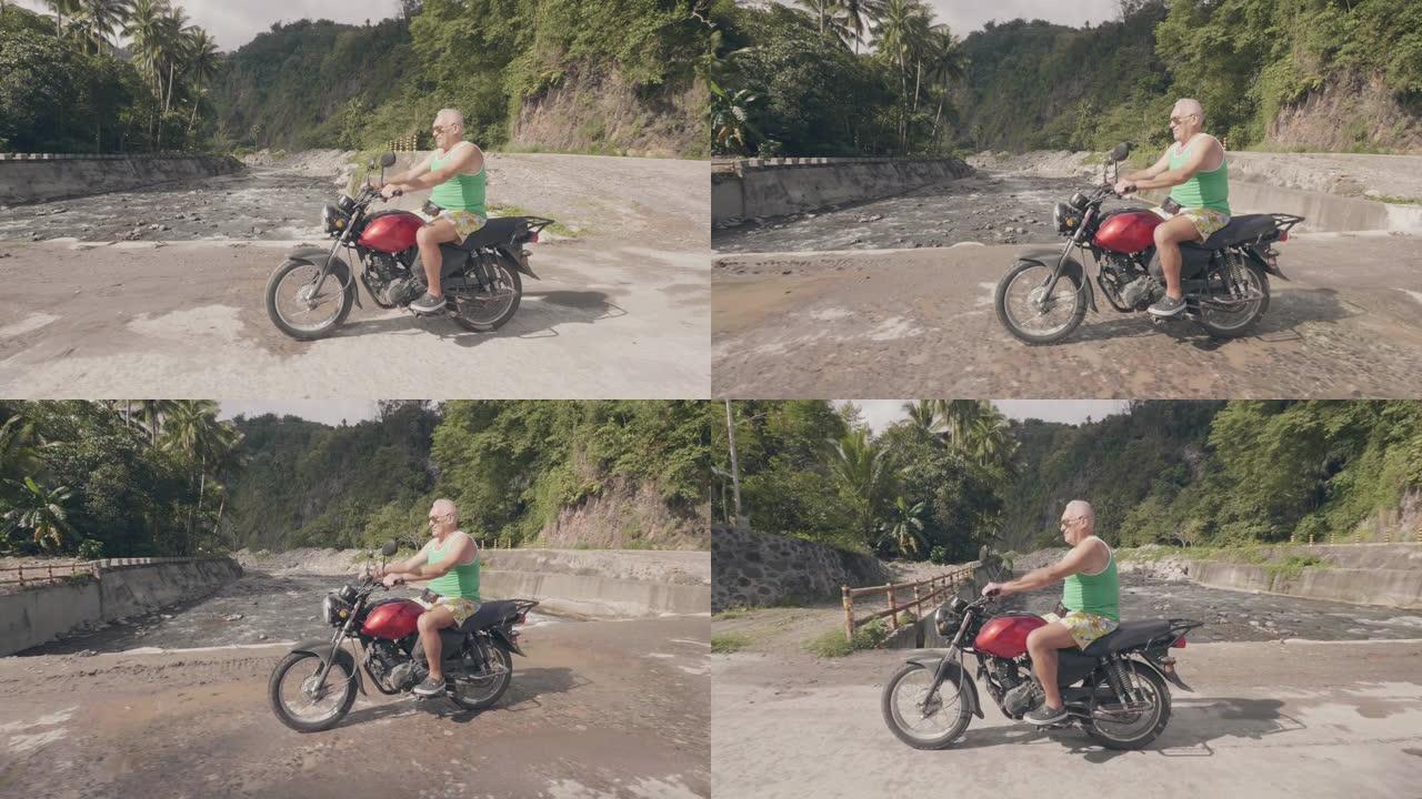 暑假期间，老人在乡村路上骑摩托车。旅行者男子在亚洲村的河桥上骑摩托车。摩托旅行。