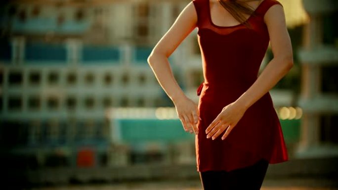 年轻漂亮的女芭蕾舞演员穿着红色连衣裙站在屋顶上-用手跳舞-明亮的日落。