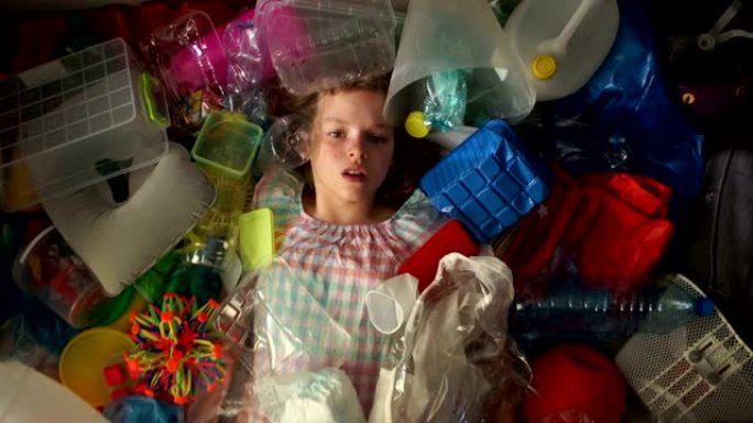 女孩躺在一堆多色垃圾中，一个塑料袋落在她身上。地球的塑料污染问题