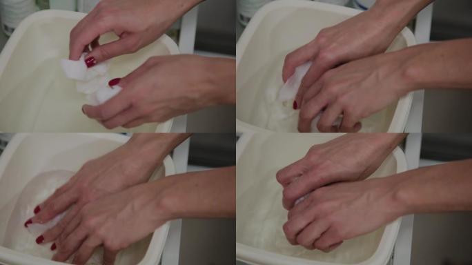 准备湿纸巾擦拭皮肤的过程。近距离的一个美容师的手。白色杯子里的水溶液。在美容院做整容手术