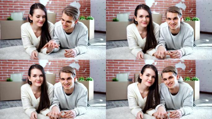 年轻的微笑夫妇手牵着手躺在地板上摆姿势，看着相机中特写镜头