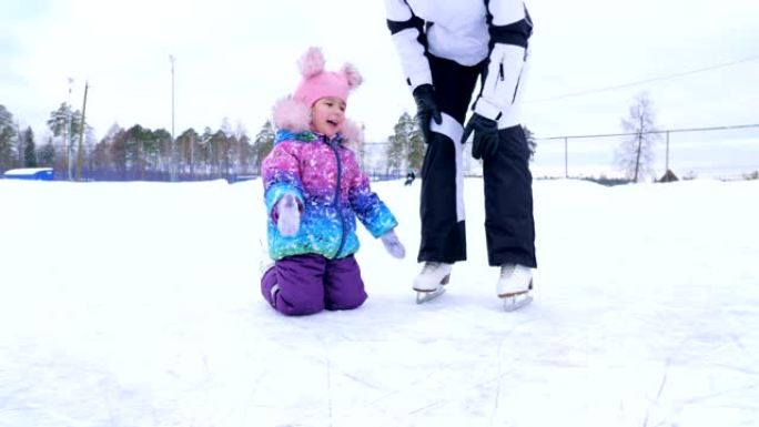 妈妈教她的小女儿在溜冰场上滑冰。