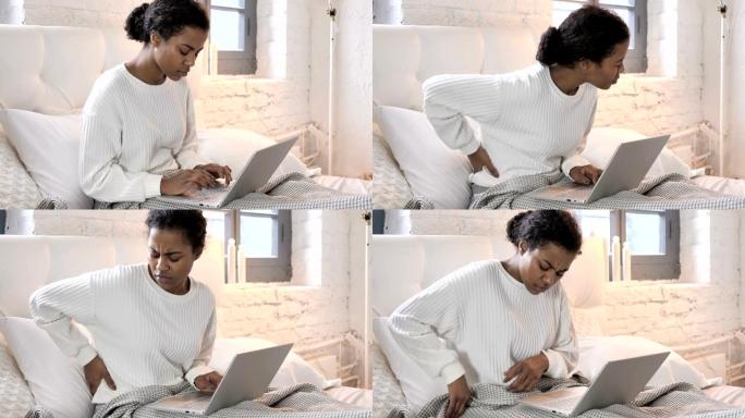 年轻的非洲妇女背痛在床上的笔记本电脑上工作