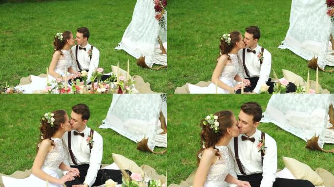 婚礼当天，新郎和新娘坐在草地上，在梳妆树和白色装饰有桌子和蛋糕的帐篷之间。