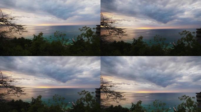 加勒比海牙买加岛蒙特哥湾大西洋上空的美丽日落的手持垂直平底锅，粉红色，橙色和蓝色的云朵，前景为树木