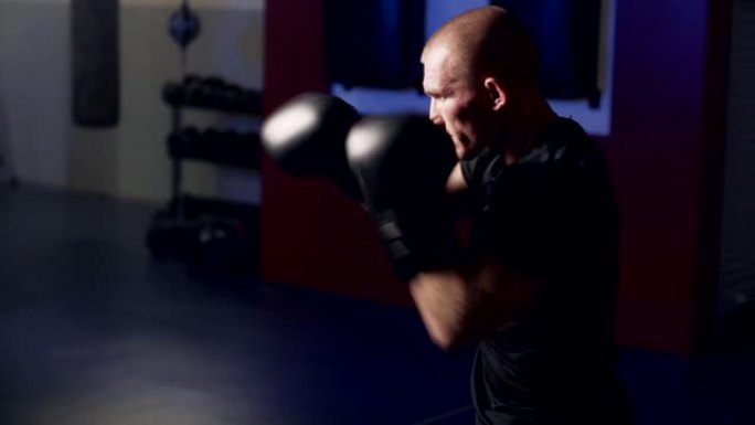 拳击手套里肌肉发达的拳击手在健身房里用阴影击打，慢动作。弱光场景