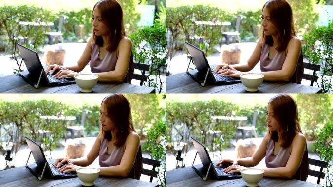 一名亚洲妇女在周末在咖啡厅工作时在笔记本电脑上打字