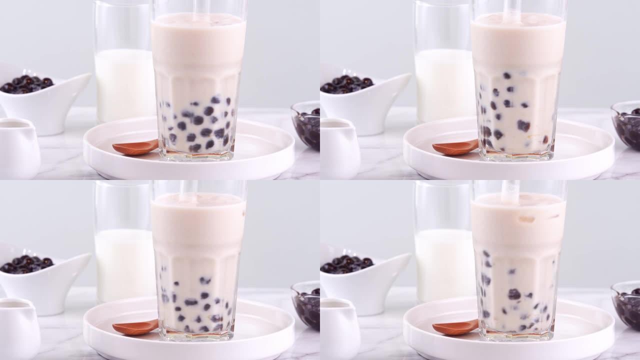 在明亮的大理石桌子白色托盘上，在玻璃杯中搅拌美味的台湾流行饮料木薯珍珠珍珠奶茶，自制概念。4k拍摄视