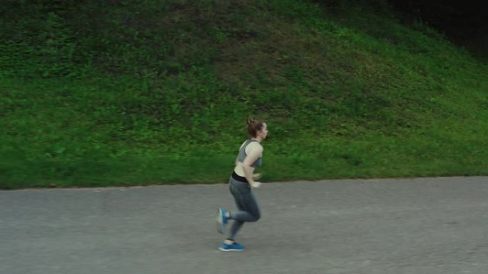 年轻迷人的女孩在城市公园跑步。女人在木头鸟瞰图中奔跑。4K，跟踪镜头