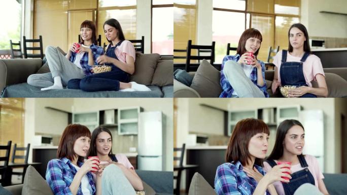 两个激动的亚洲和高加索女性朋友坐在家里的沙发上，观看连续剧，电视节目或电影的照片。他们的男朋友在阳台