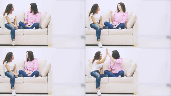 在温暖的家庭环境中，两个女朋友坐在沙发上聊天，给了五个，微笑着。