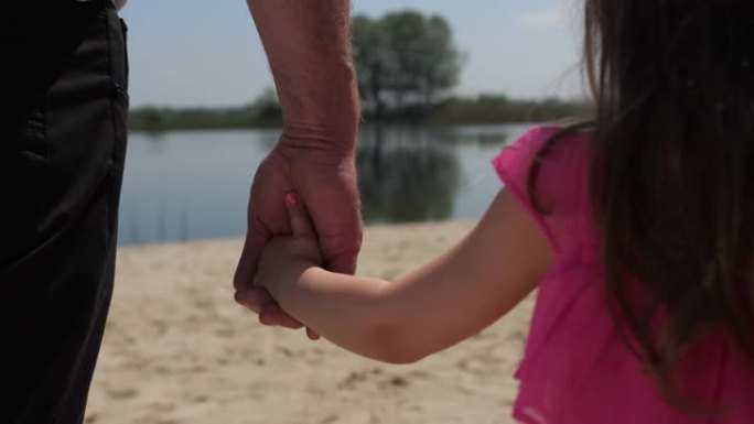 特写。孙女牵着祖父的手。他们前进。沿着湖边散步。4k慢速移动
