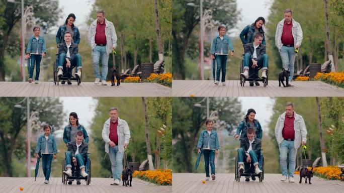 一个秋天的下午，一个充满爱心的家庭和一个残疾少年在公园里散步。坐在轮椅上的年轻人与狗和父母在公园里度