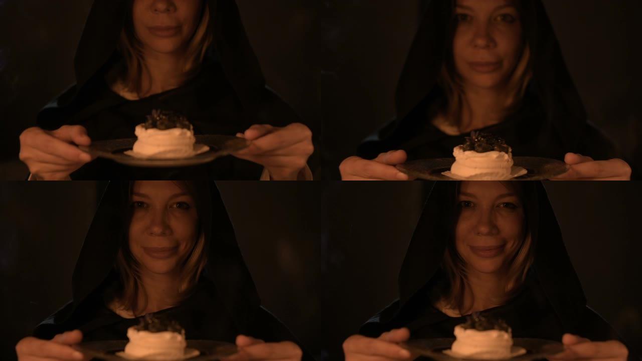一个心满意足的女孩魔术师在黑暗的房间在烛光下变魔术自己一个蛋糕的特写。拿着一盘蛋糕低调的现场摄像机。