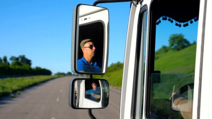 太阳镜中的卡车司机反射在行驶中的汽车侧镜中。男子驾驶卡车通过乡村路骑行到目的地。货物运输概念。背景模