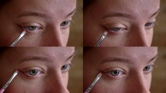 年轻的高加索女化妆师在她的下眼睑上使用刷子的特写肖像