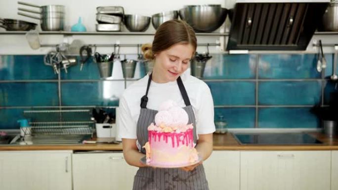 快乐的女性糖果厨师看着手工制作的点滴蛋糕，上面装饰着酥皮和奶油糖霜，欣赏它站在餐厅厨房，中等锁定镜头