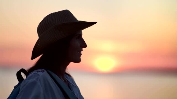 愉快的游客潮女戴着帽子享受自由，欣赏美丽的日落在海边的观点