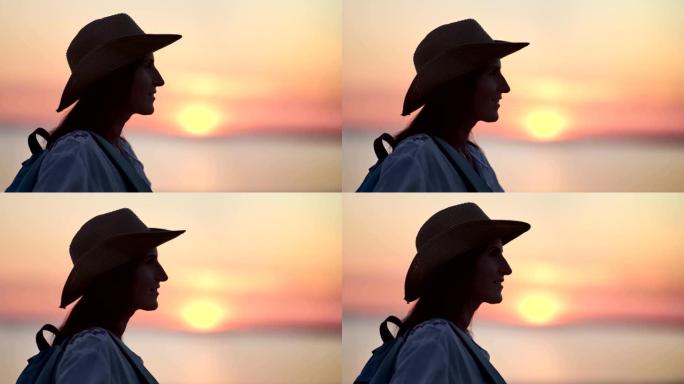愉快的游客潮女戴着帽子享受自由，欣赏美丽的日落在海边的观点