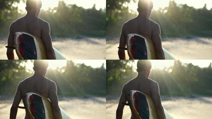 日出时海滩上一个漂亮的年轻冲浪者的后视图