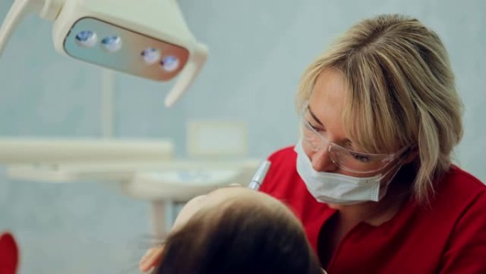 漂亮的中年女人对待牙齿女孩。牙医在现代牙科诊所为病人钻了一颗牙。肖像视图。