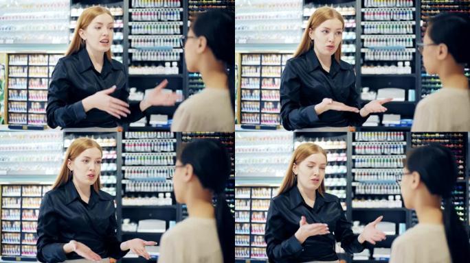 美丽自信的女售货员中照片，红发描述产品，向艺术商店的亚洲顾客解释差异