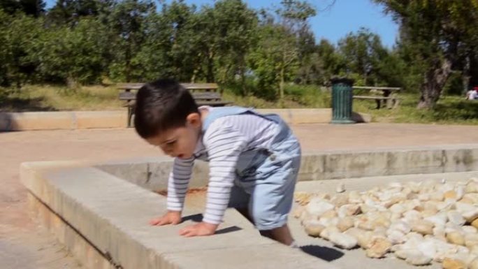 可爱的两岁男孩在公园玩石头