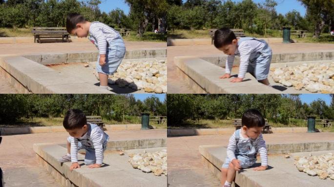 可爱的两岁男孩在公园玩石头