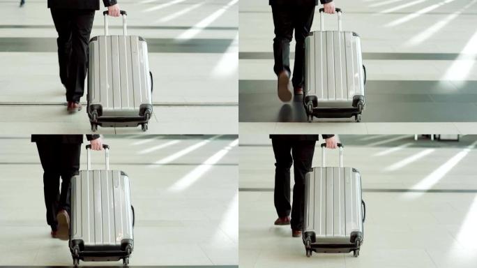 跟随无法识别的商人沿着机场大厅行走并拉着手推车手提箱的中等镜头