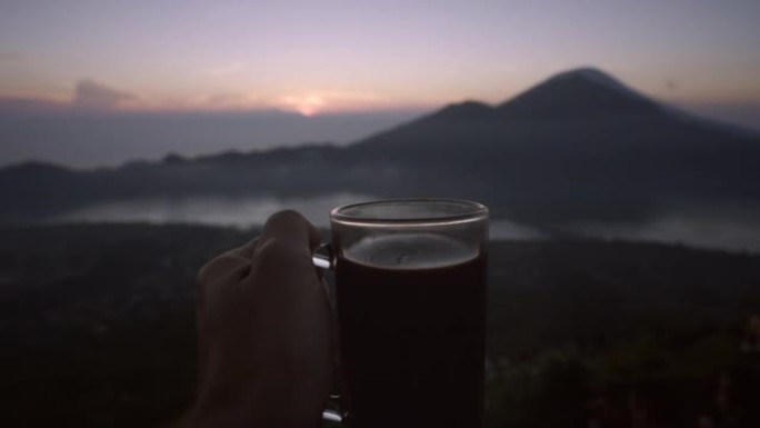 男子手握着火山背景上的热咖啡玻璃