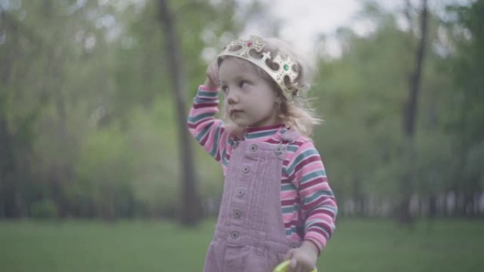 可爱的小女孩在她头上的皇冠在前景，绿色公园在背景。