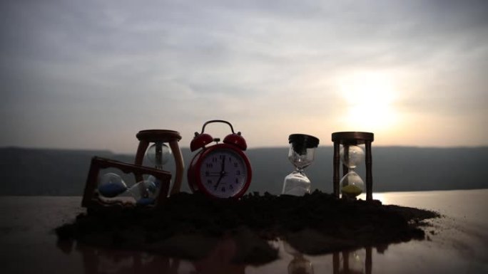 时间概念。日落时沙漏时钟和烟雾在模糊的自然背景上的剪影，或烟雾下的时间符号，时间结束或爱情结束。乐观