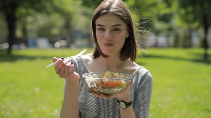 女人坐在夏季公园吃新鲜沙拉
