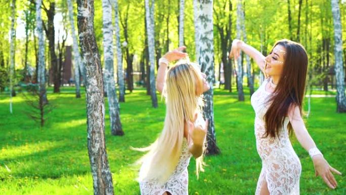 穿着类似服装的金发和黑发女人在阳光普照的公园跳舞