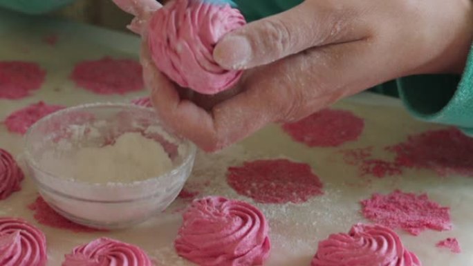 一个女人用刷子将糖粉涂在棉花糖上。接下来是不同色调的准备好的棉花糖。