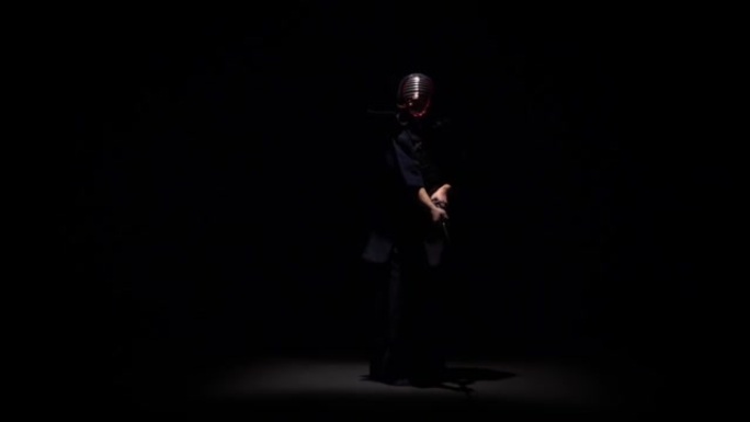 剑道战士在聚光灯下的黑暗工作室用武士刀表演武术。慢动作